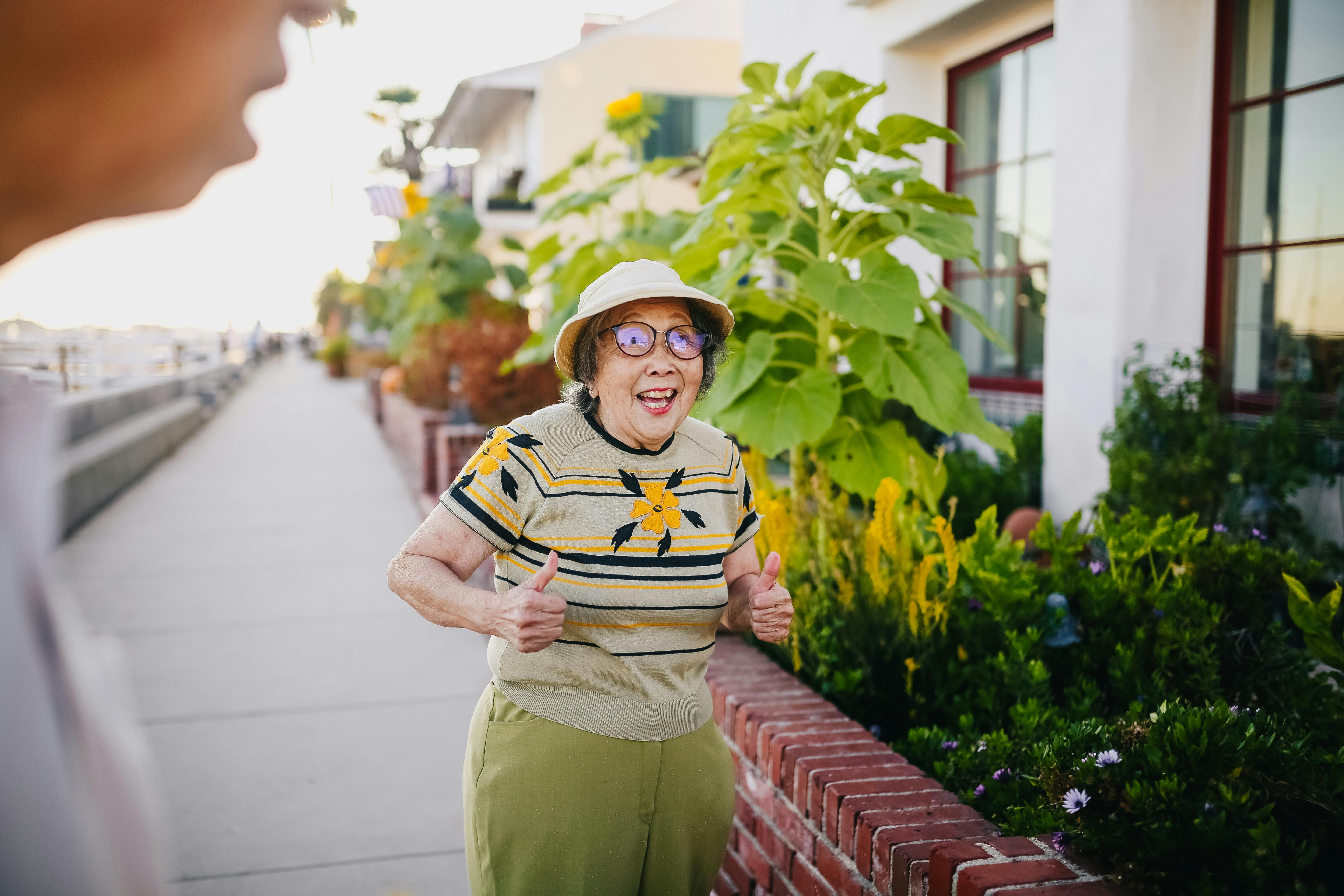Free Elderly woman with thumbs up, happy in a garden setting during the day. Stock Photo
