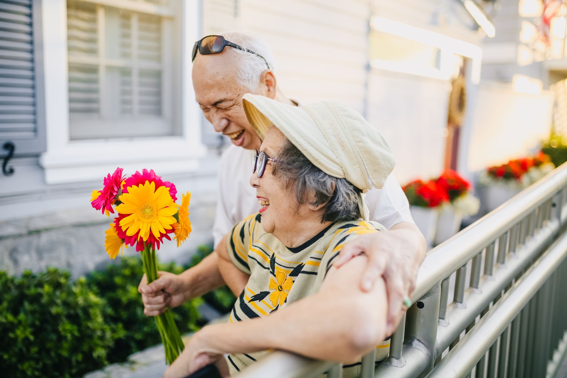 Asian elderly couple holding flowers and smiling together outdoors.