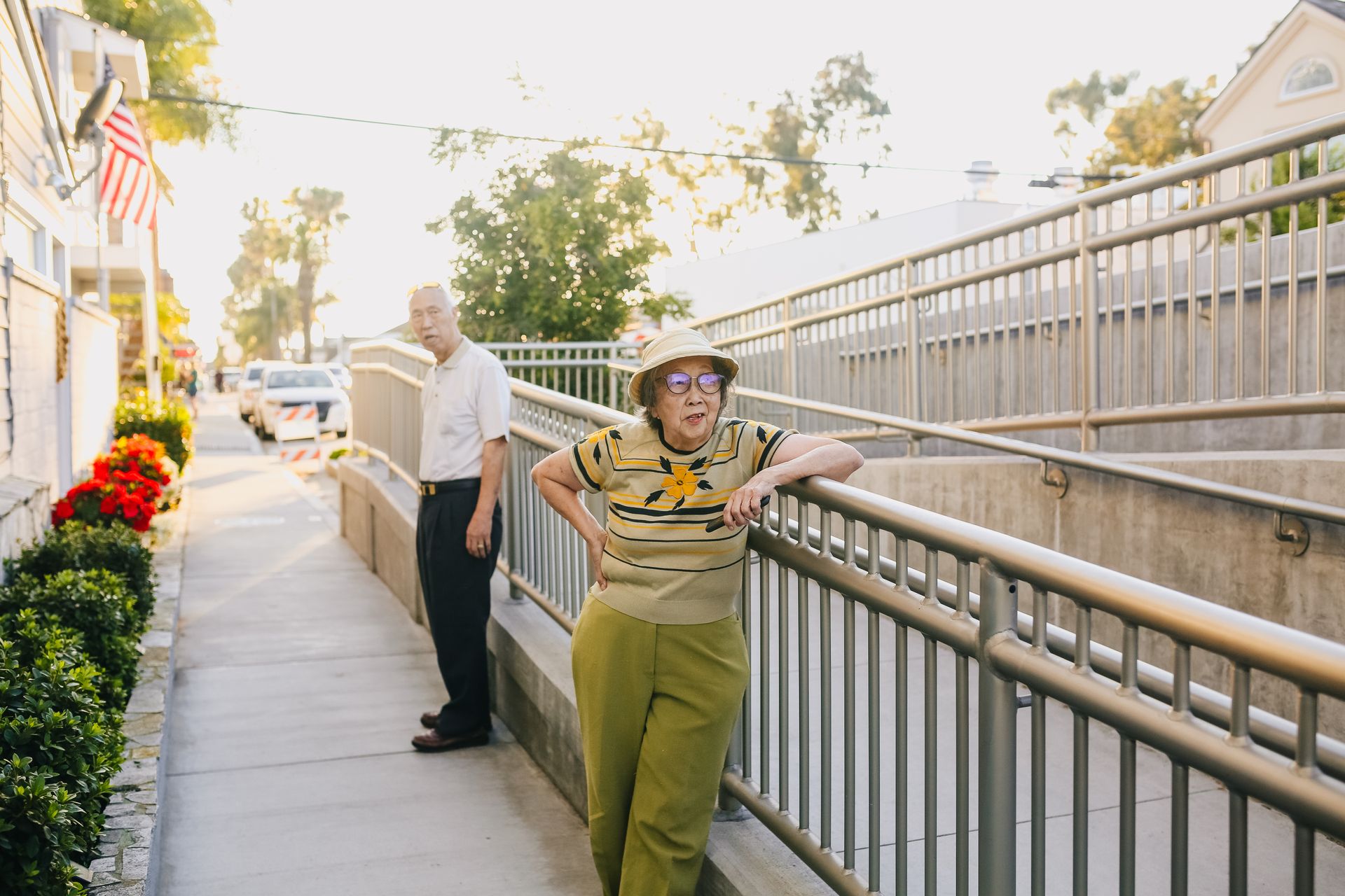 Elderly Asian couple relaxing outside near a railing during a sunny day.