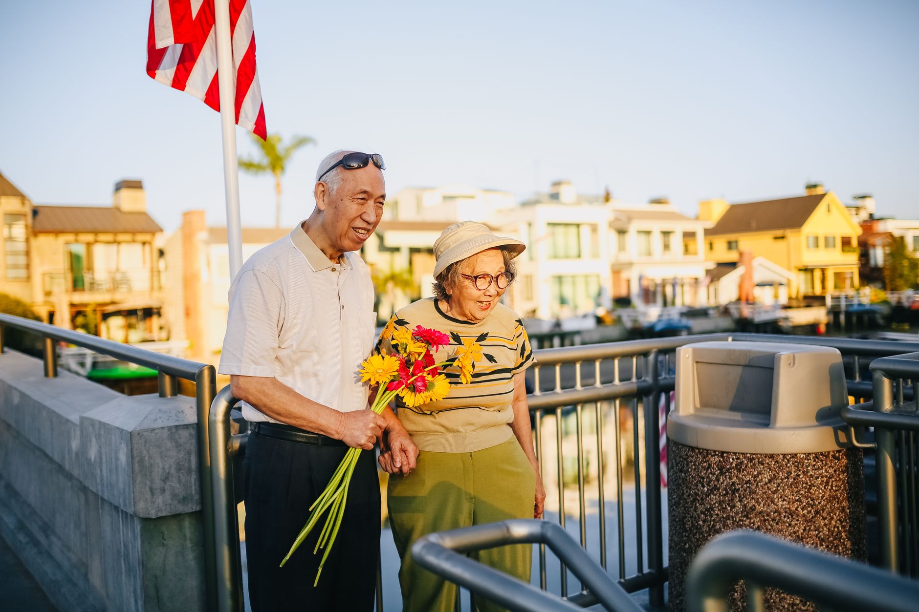 Elderly Asian couple holding hands with flowers, enjoying a sunny day outdoors.