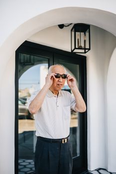 一位穿着休闲装的老人正在现代建筑外调整太阳镜