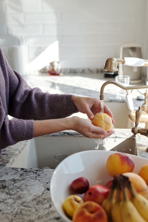 Free Close-up of hands washing a peach under running water in a sunny kitchen. Stock Photo