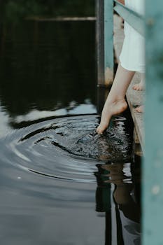 Close-up of a person's bare foot gently dipping into a calm lake, creating ripples.