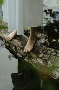 一位赤脚妇女站在池塘边的木头上，四周环绕着大自然，环境宁静