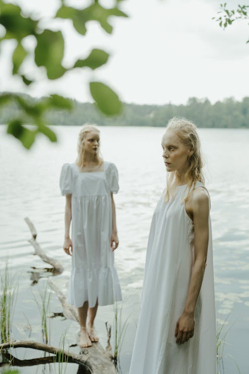 Blonde Women in White Dresses Standing on Lakeshore