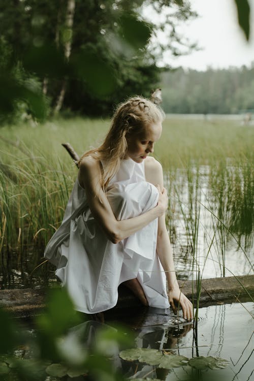 Blonde Woman in White Dress Crouching on Lakeside