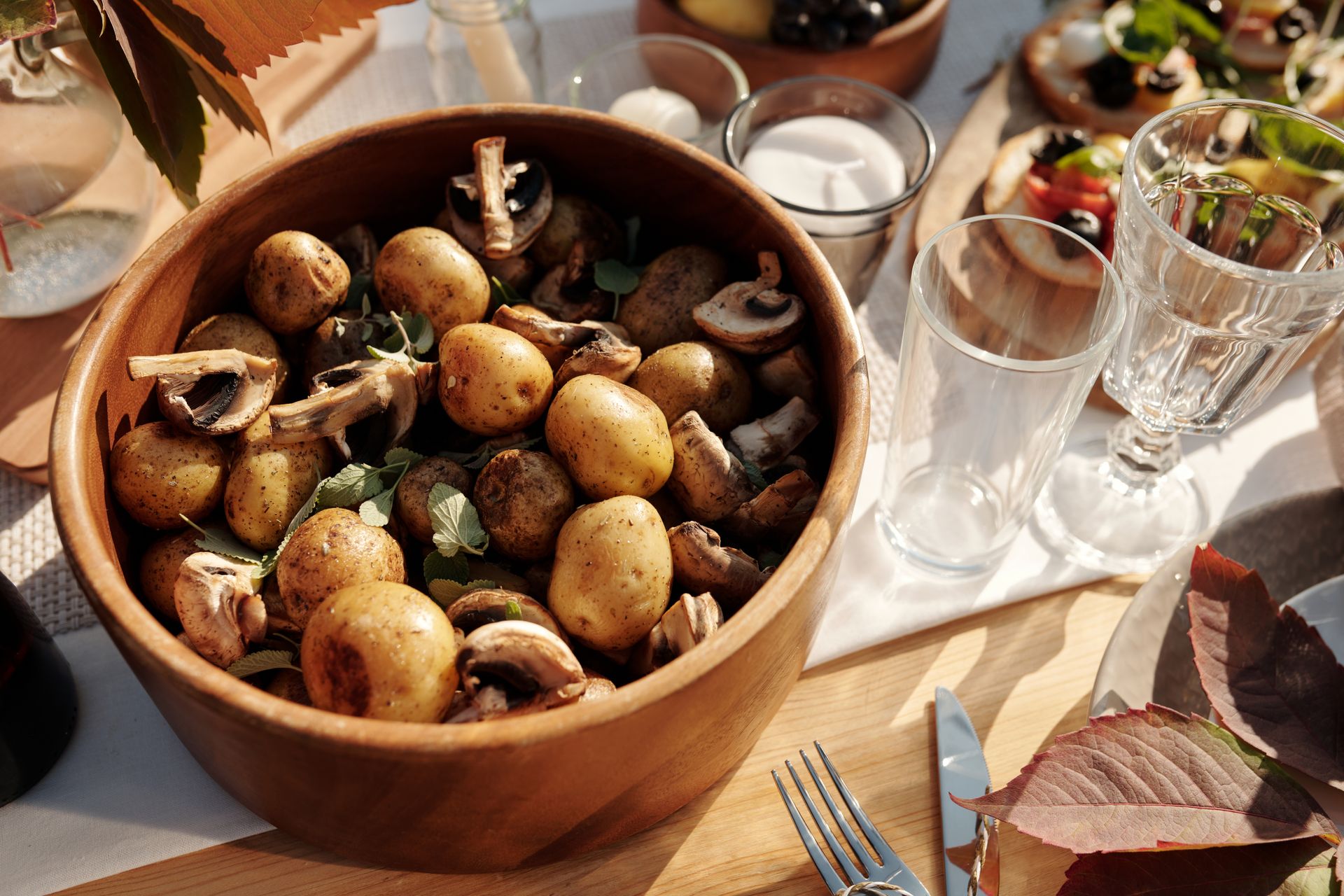 A rustic bowl of baby potatoes and mushrooms on a sunny dining table setting.