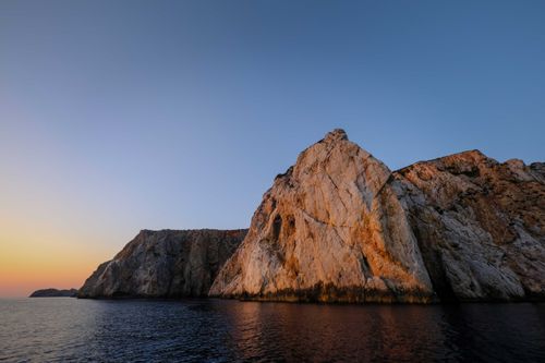 Free Spectacular view of dry rough rocks reflecting in rippled sea with horizon at sunset Stock Photo