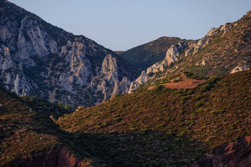 Picturesque view of high rough mountains with growing grass on irregular surface in soft sunlight