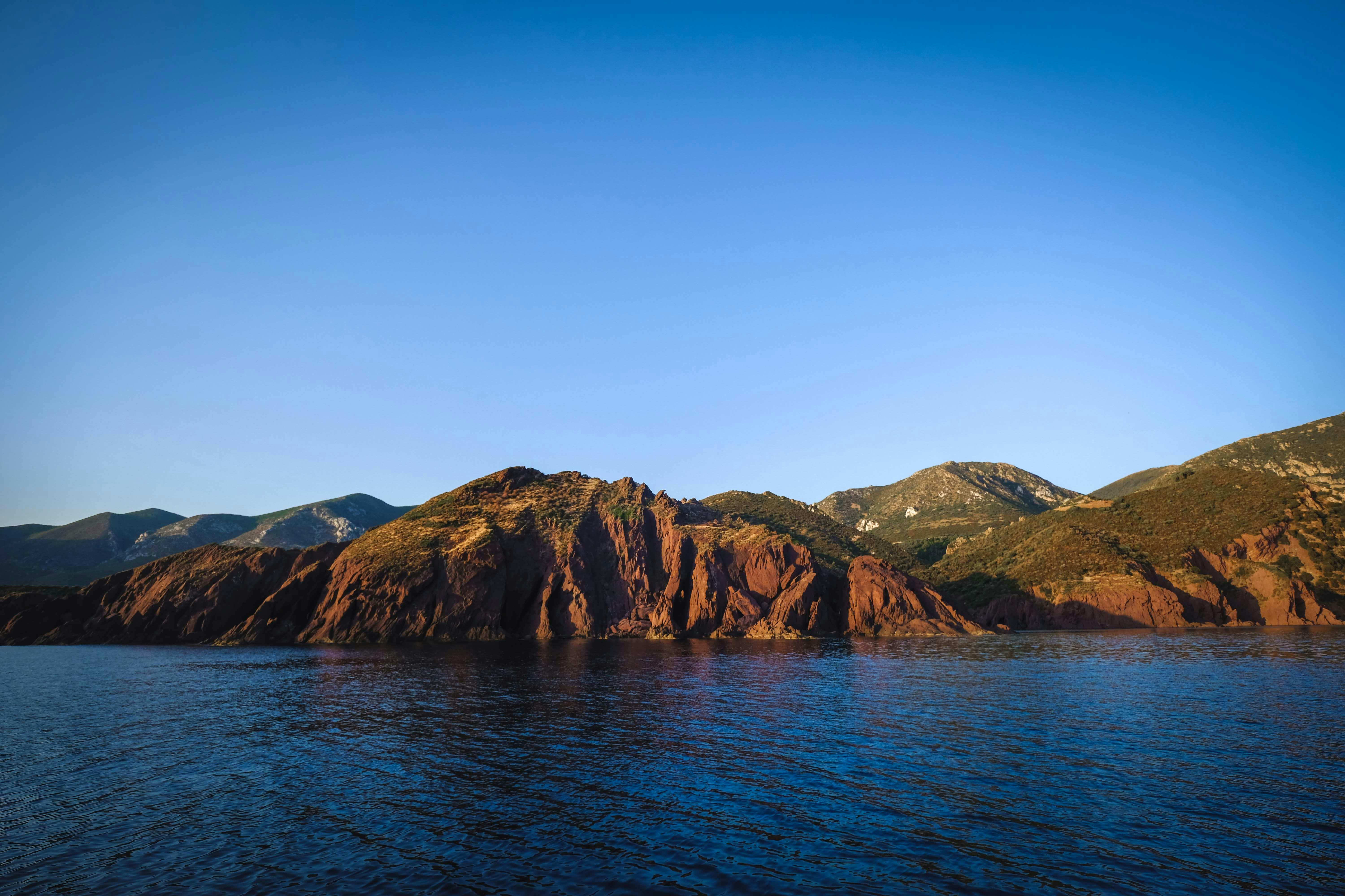 green mountains against ocean under bright sky