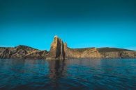 Rocky formations reflecting in sea under blue sky