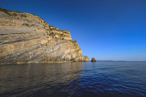 Scenic view of high dry mount against wavy ocean under colorful sky in daylight