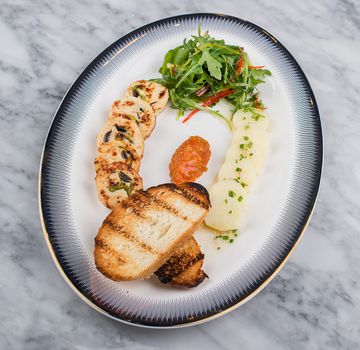 Elegant gourmet dish featuring grilled bread, salad, potatoes and chutney on a ceramic plate.
