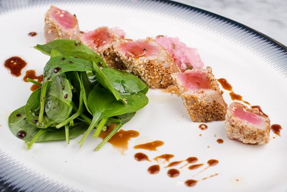 Sliced sesame-crusted seared tuna with rare pink centers, baby spinach, pickled ginger and dark glaze