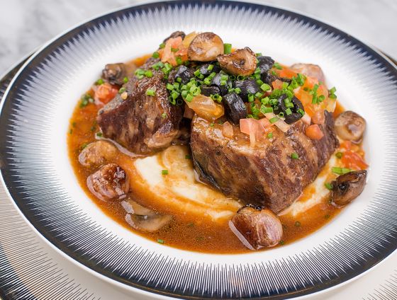 Braised beef short ribs on mashed potatoes with mushrooms, black olives, diced tomato and chives