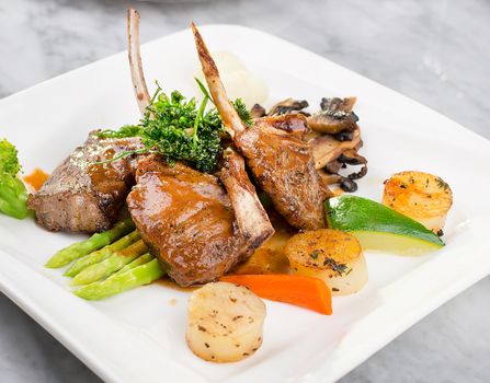 Delicious lamb chops with vegetables plated elegantly on a marble surface.
