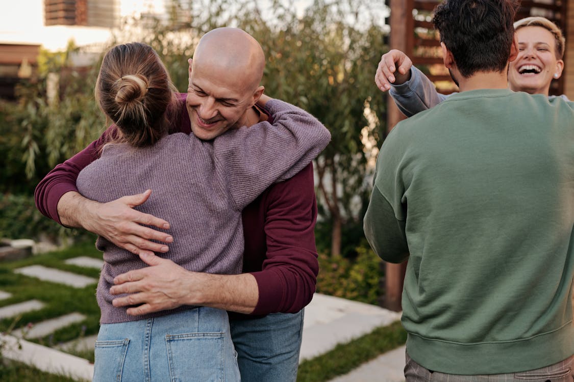 Cheerful friends hugging and smiling while spending time together in suburban yard during weekends