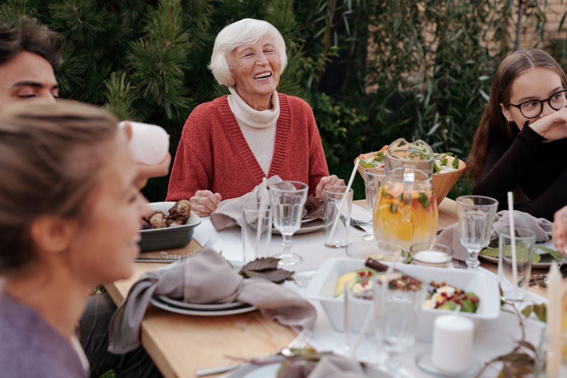 Free Smiling elderly woman with family and friends enjoying dinner at table backyard garden Stock Photo