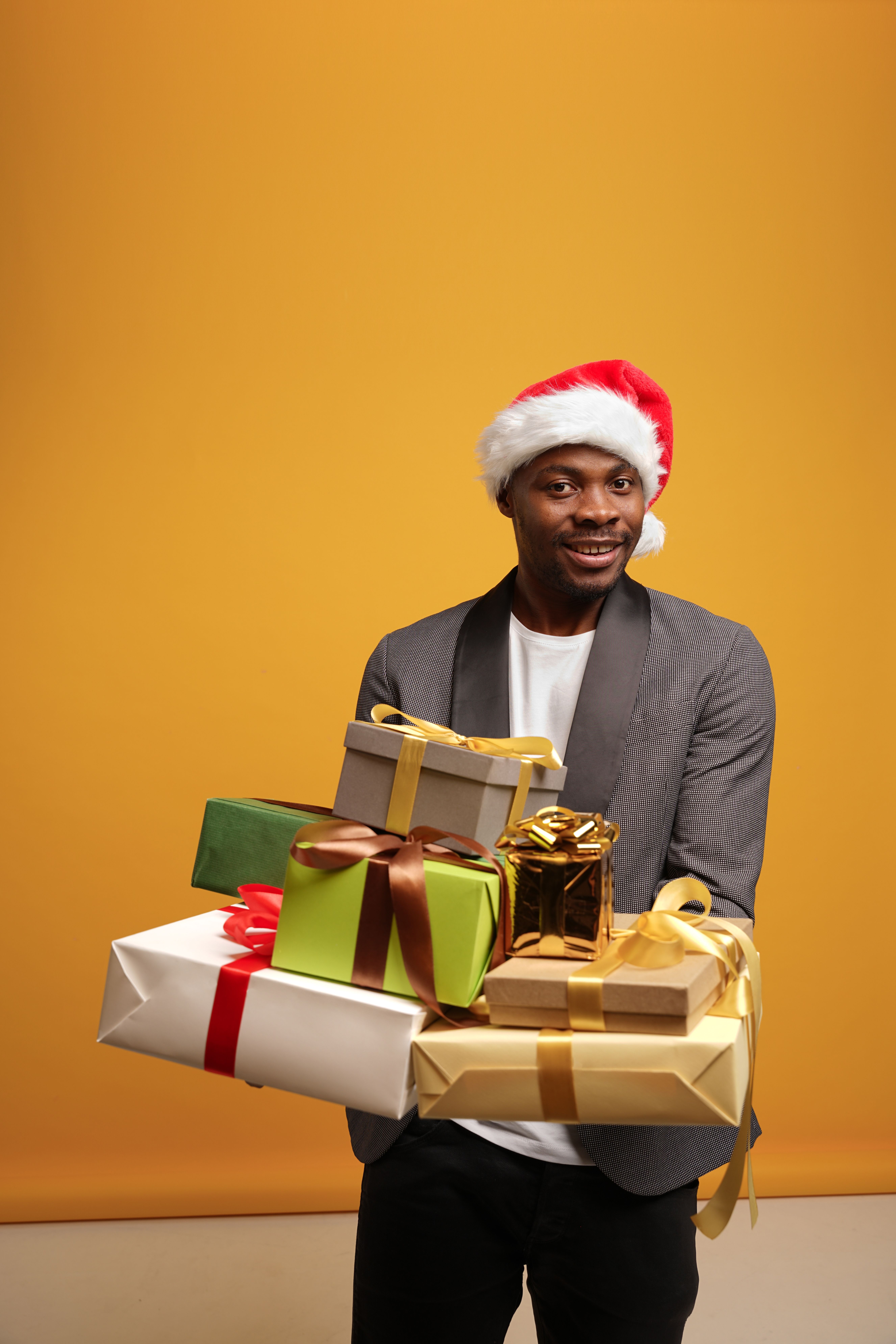 Joyful man in Santa hat holding Christmas gifts, set against a yellow background.