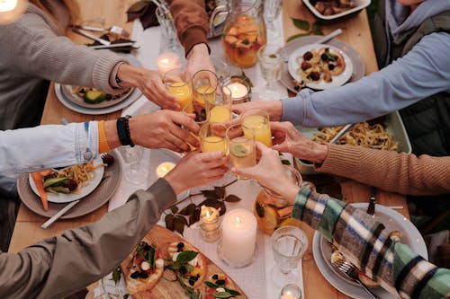 Free From above of crop friends enjoying dinner with candles while cheering with glasses of drinks Stock Photo