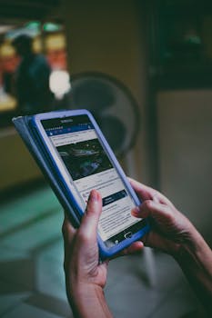 Crop faceless person browsing social media on modern tablet on blurred background in light room