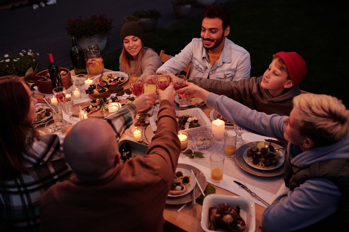 Free From above multiethnic people with children spending evening at dinner in dusky garden and cheering with drinks Stock Photo