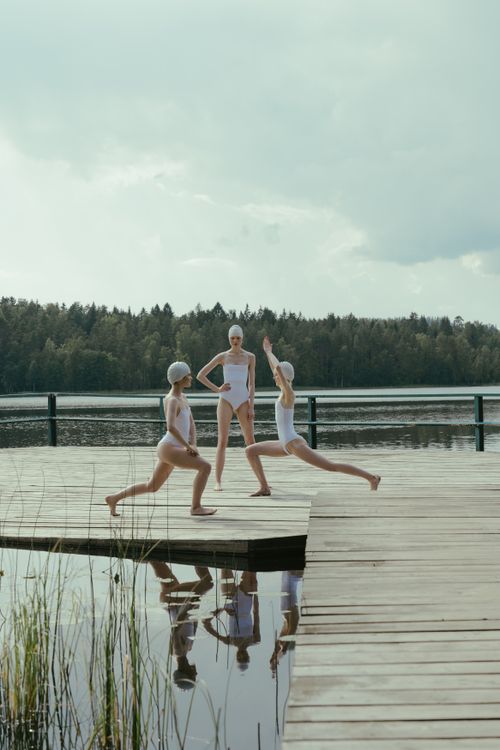 Free Three women practicing yoga on a peaceful lakeside pier, fostering tranquility with nature. Stock Photo