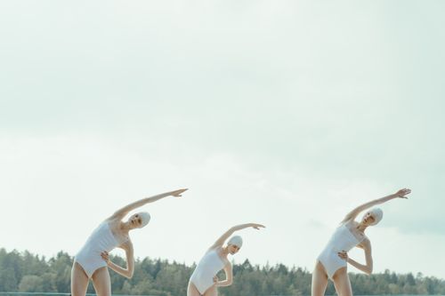 Free Three women in white swimsuits performing synchronized stretching exercises outdoors. Stock Photo