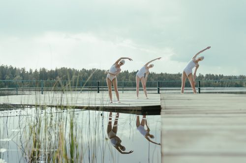 Free Three women practicing stretches on a lakeside pier, emphasizing fitness and tranquility. Stock Photo