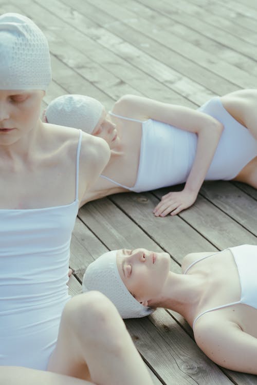 Women Wearing White Swimwear Lying on a Wooden Floor