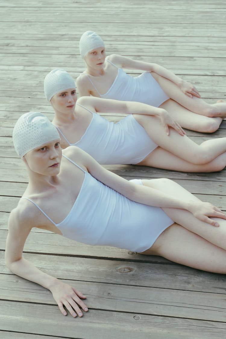 Three Women Wearing White Swim Wear Lying On A Wooden Floor