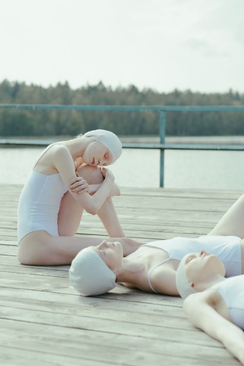 Free Three women in swimwear peacefully resting by a lakeside pier under a clear summer sky. Stock Photo