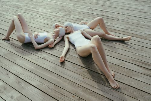 Free Three women in white swimwear lying on a wooden deck, eyes closed, under sunny skies. Stock Photo