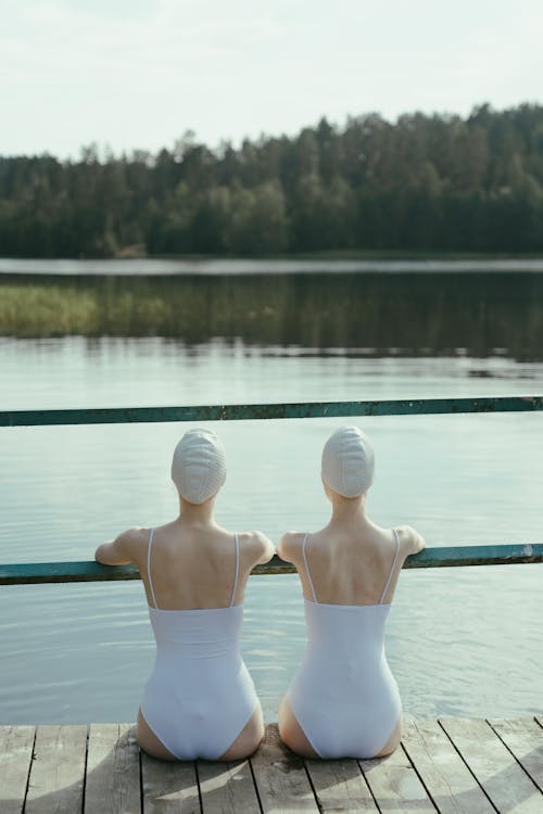 Two Persons in White Swimsuits Sitting on the Dock