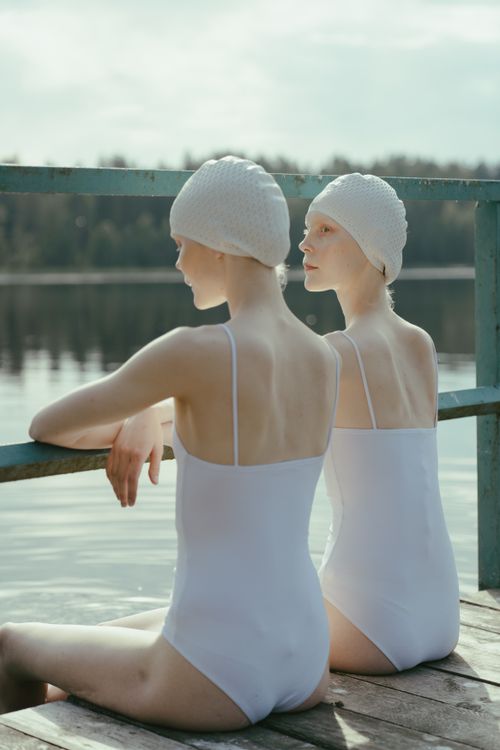 Free Two women in swimwear and caps sitting by a tranquil lake on a wooden dock. Stock Photo