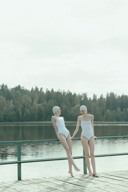 Free Two women in white swimsuits enjoying a sunny day by a tranquil lake. Stock Photo
