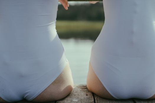 两名身穿白色泳衣的女子坐在码头上，欣赏着宁静的湖景