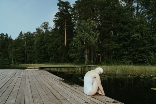 Free Woman relaxing on a lakeside wooden dock surrounded by lush greenery, embracing tranquility. Stock Photo