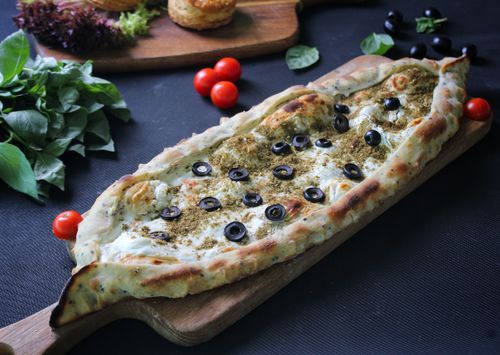 Free Savory Turkish pide topped with black olives on a wooden board, garnished with basil and tomatoes. Stock Photo