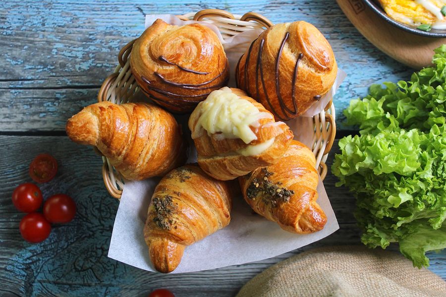 A selection of freshly baked croissants in a basket, surrounded by vibrant ingredients, ideal for food photography.