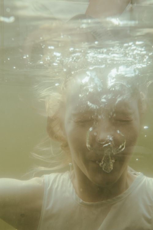 Free A girl submerged underwater with air bubbles around her face in a close-up shot. Stock Photo