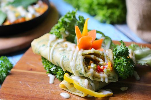 Flavorful vegetable wrap on wooden board with fresh greens and creamy sauce.