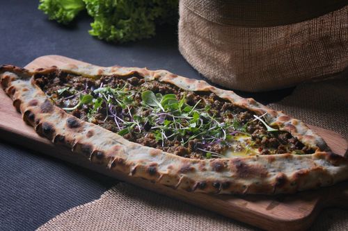 Free A freshly baked Turkish pide topped with ground meat and fresh greens, presented on a wooden board. Stock Photo