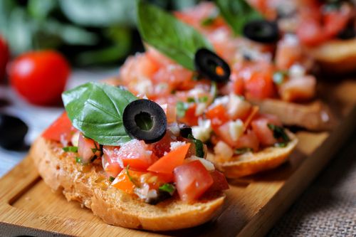 Free Close-up of Italian bruschetta topped with basil, tomatoes, and black olives on wooden board. Stock Photo