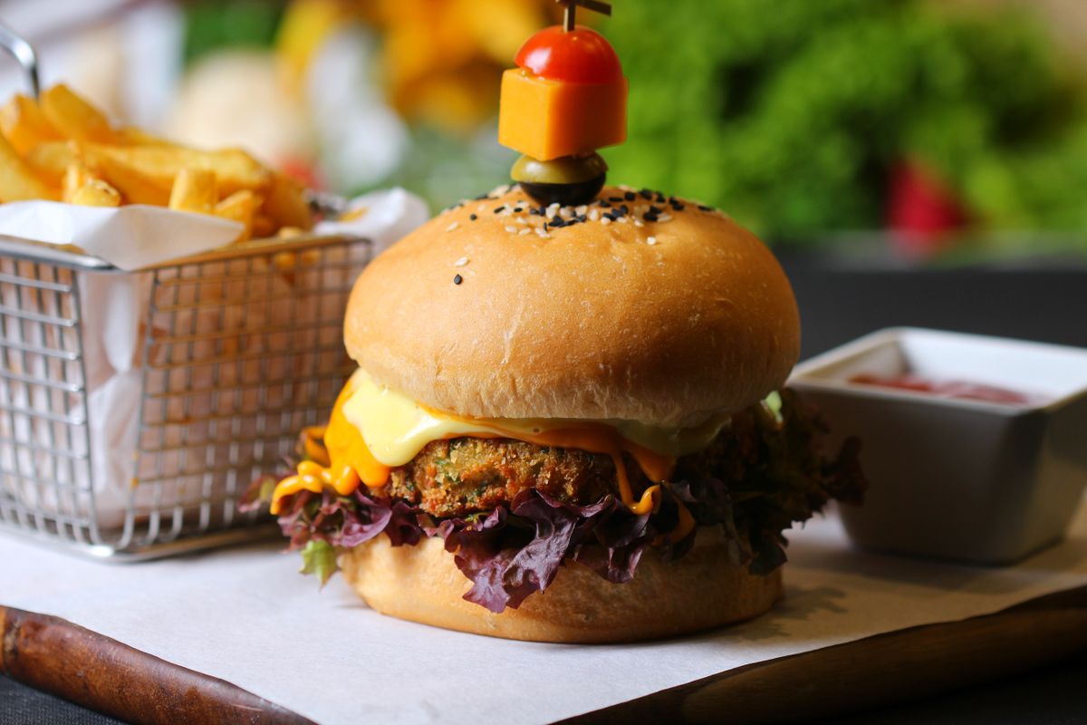 Veggie patty burger with melted cheese, red lettuce and spicy mayo beside a fries basket