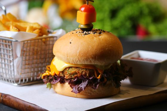 Veggie patty burger with melted cheese, red lettuce and spicy mayo beside a fries basket
