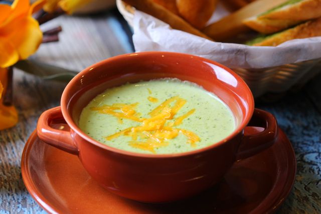Close-up of creamy broccoli soup in a terracotta bowl with cheddar garnish.