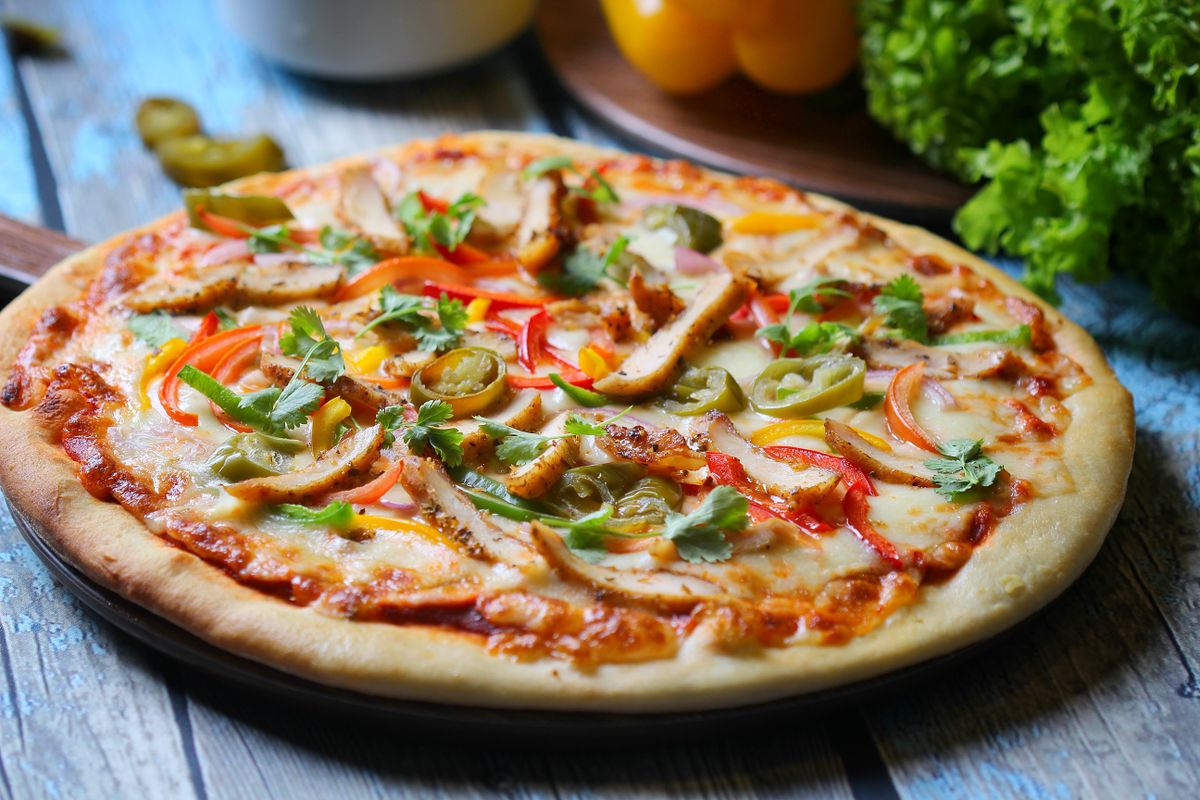 Chicken pizza topped with bell pepper strips, pickled jalapeno slices, melted cheese and cilantro