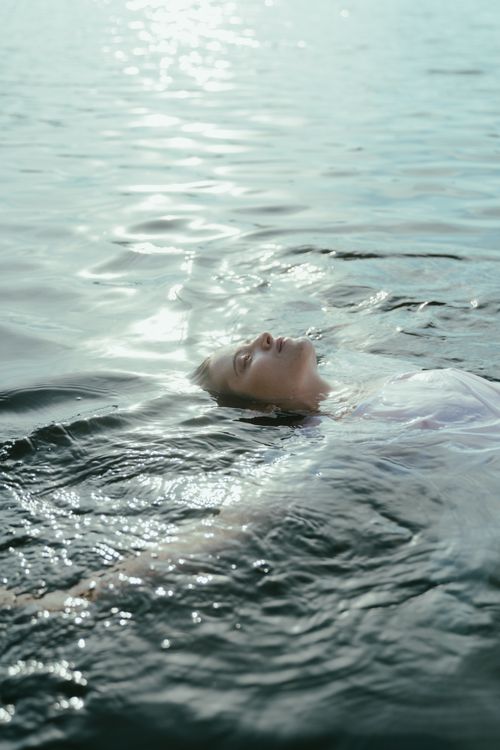 Free A peaceful scene of a woman in a white dress floating on a serene lake during daytime, capturing tranquility and freedom. Stock Photo