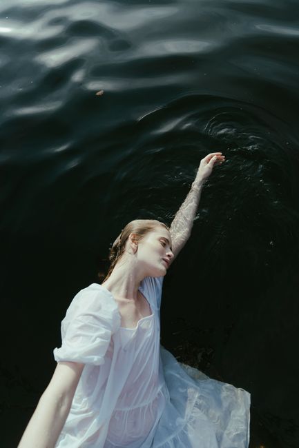Elegant woman in white dress gracefully floating on dark water, creating a serene and artistic scene.